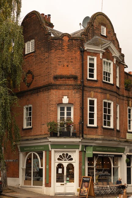 The image depicts a historic three-story red-brick building situated on a street corner, with a ground-floor shop featuring green awnings and large display windows. The upper floors include multiple w